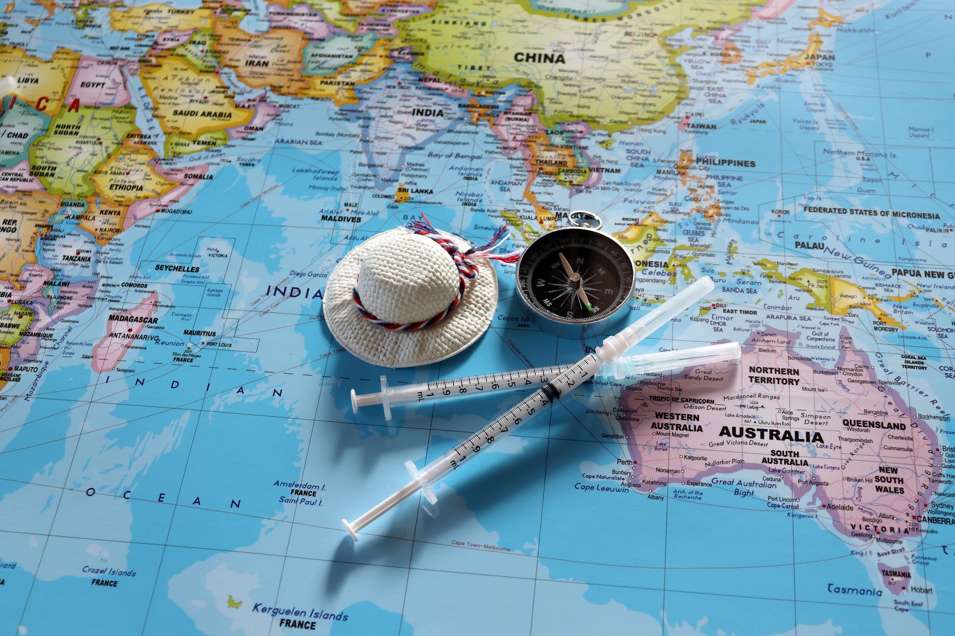 A compass with two disposable syringes and travel cap on world map.