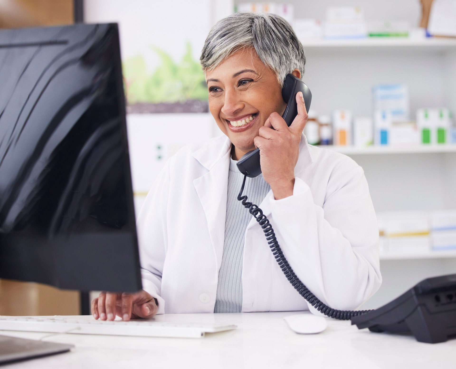 Pharmacist, telephone and computer for prescription with woman in conversation for retail healthcare. Chemist, working and pharmacy on computer with customer service or medicine with telehealth.