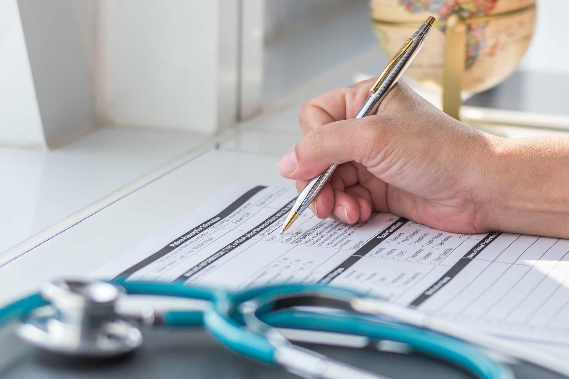 Doctor writing on a medical record or prescription form at a clinic desk with a stethoscope in view—representing professional healthcare services like patient assessments and treatments available under the Pharmacy First scheme at Chartwell Pharmacy in Southampton.