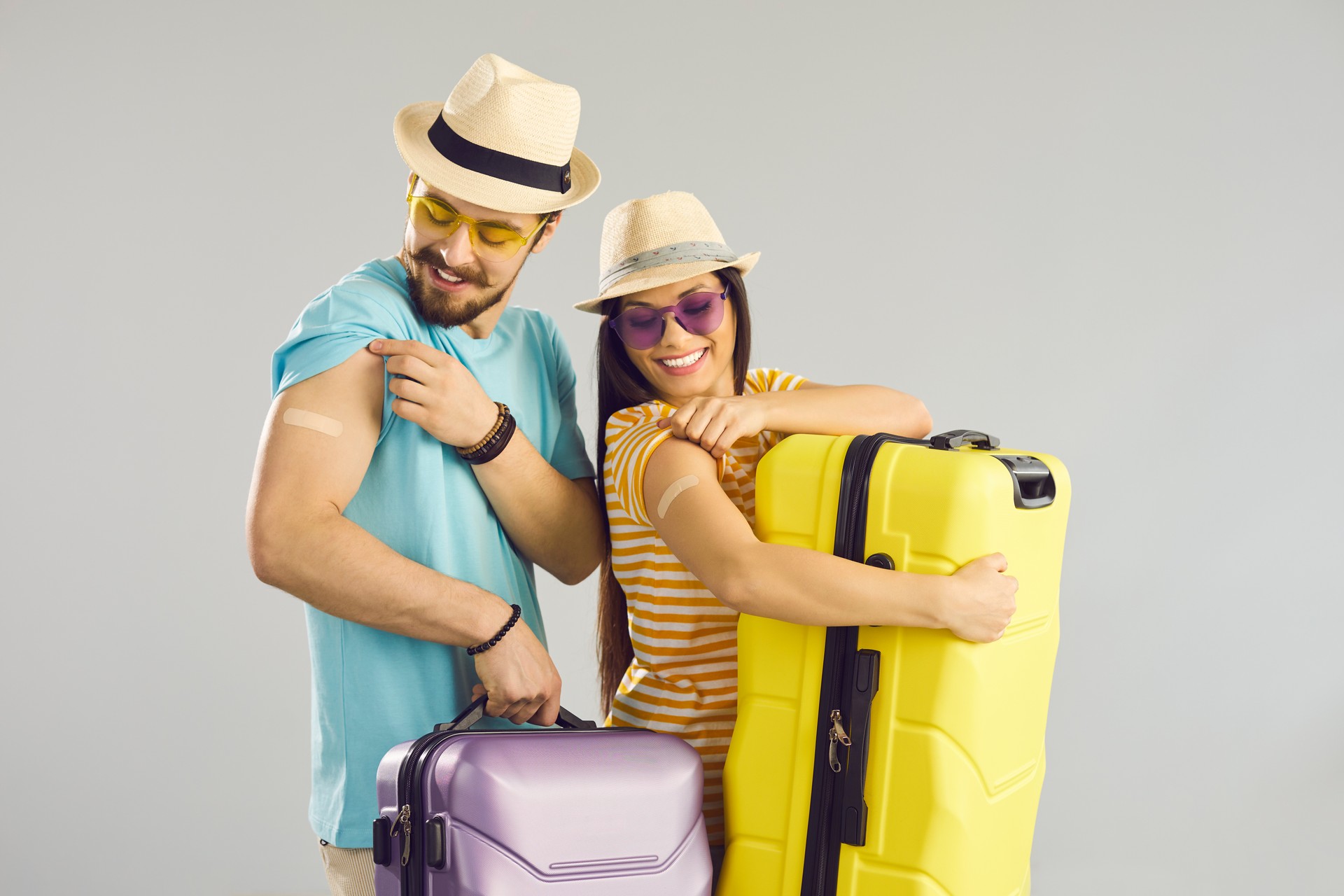 Happy young couple holding suitcases and showing arms after getting Covid-19 shot