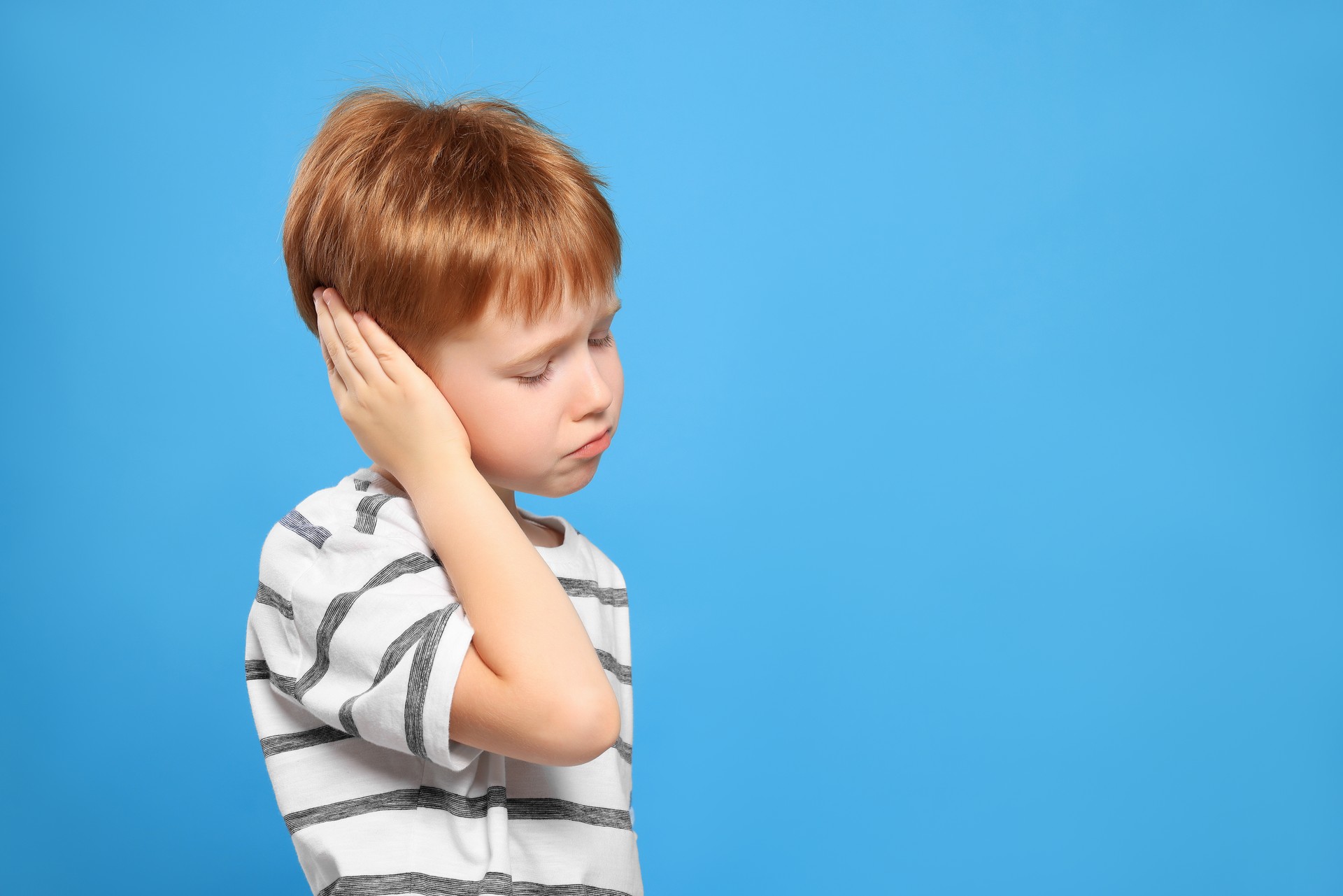 Little boy suffering from ear pain on light blue background. Space for text